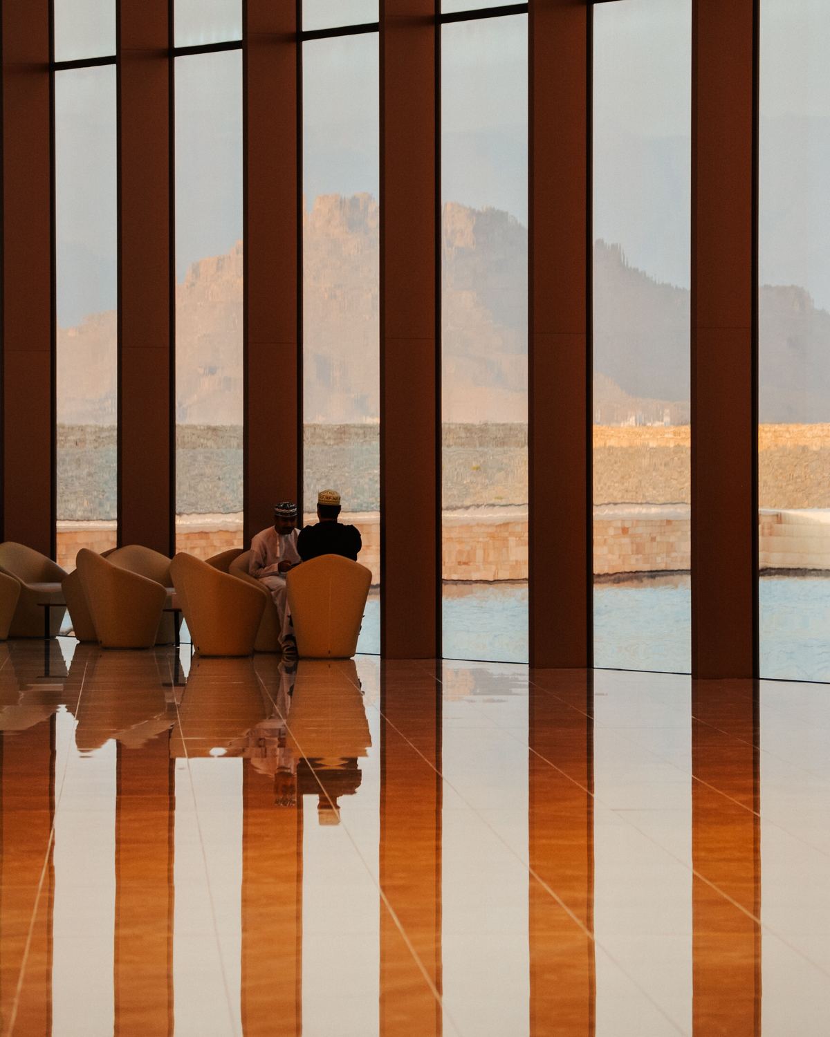 Two people seated by a window facing mountains in Manah, Oman